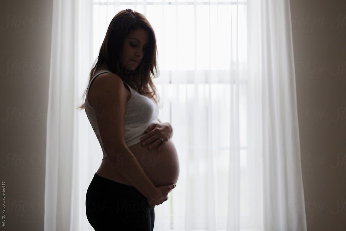 Silhouette of Pregnant Woman with hands on belly in Window