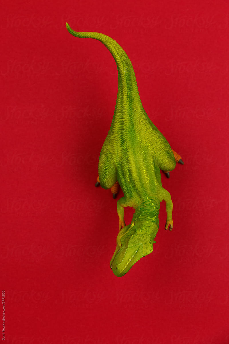 Small green toy dinosaur on red background