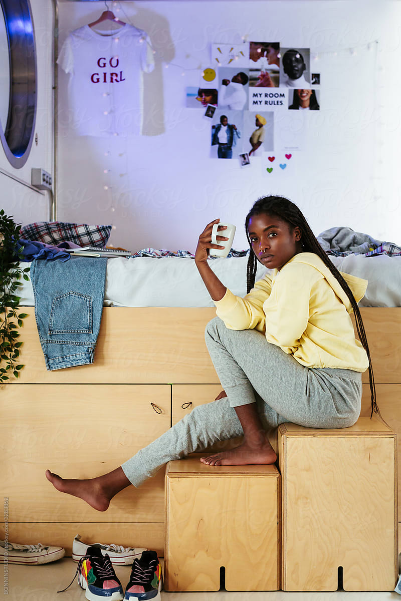 Black teenager with mug near bed