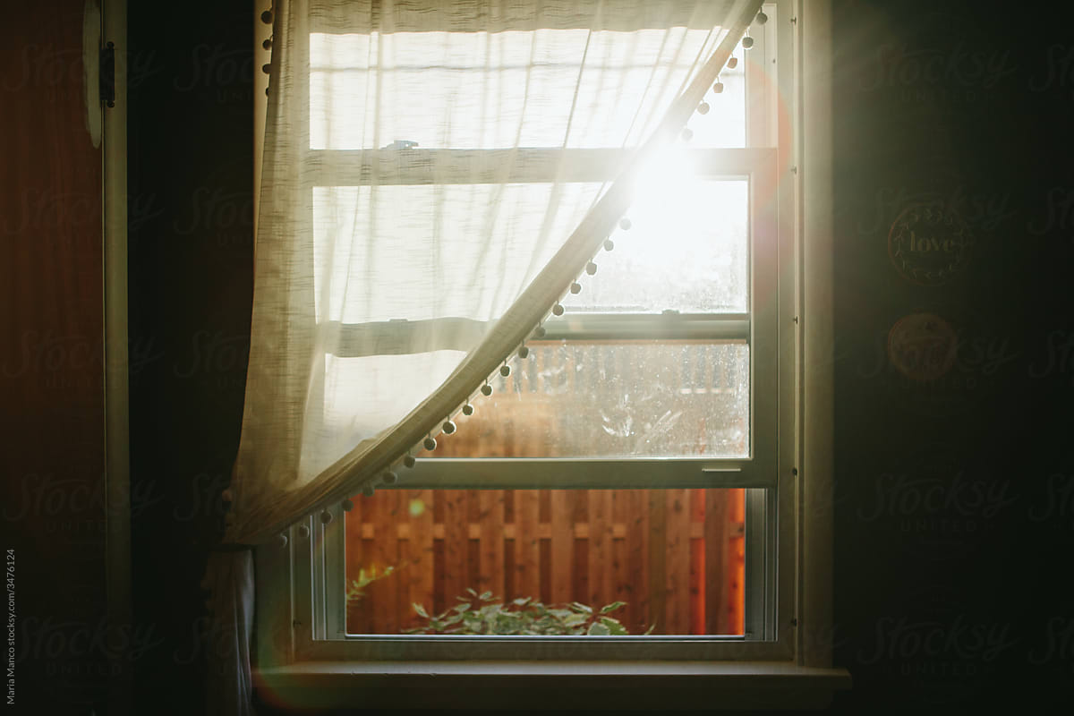 Window from inside home being illuminated by sunlight illuminating sheer curtain