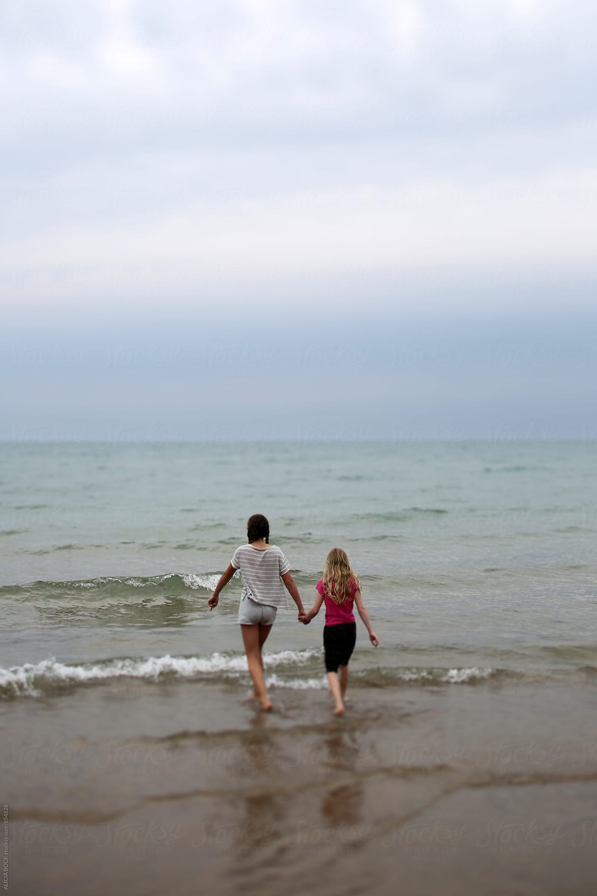 Two Girls Holding Hands Walking Out Into The Water