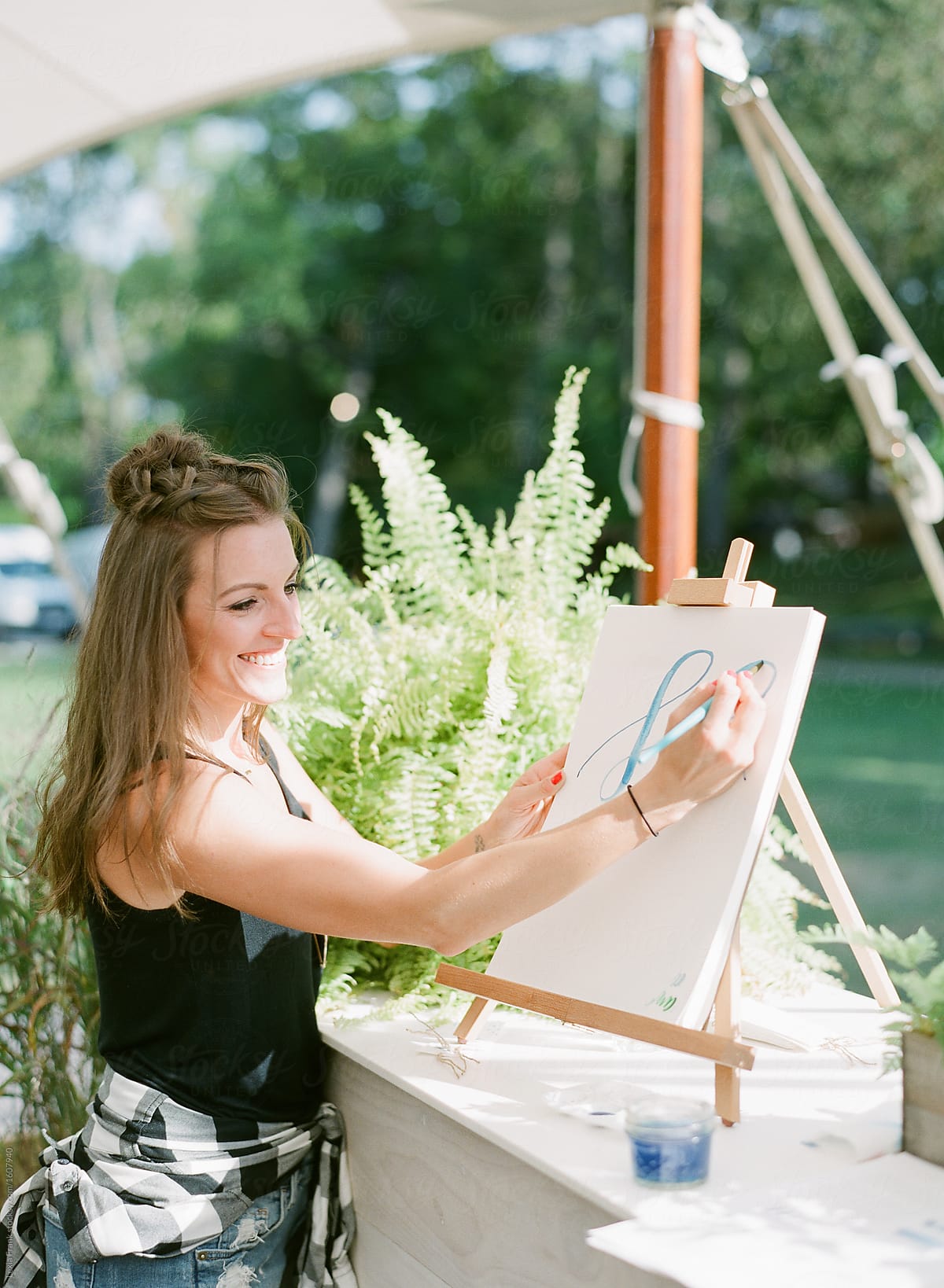 woman demonstrates watercolor lettering on easel outside in the summer