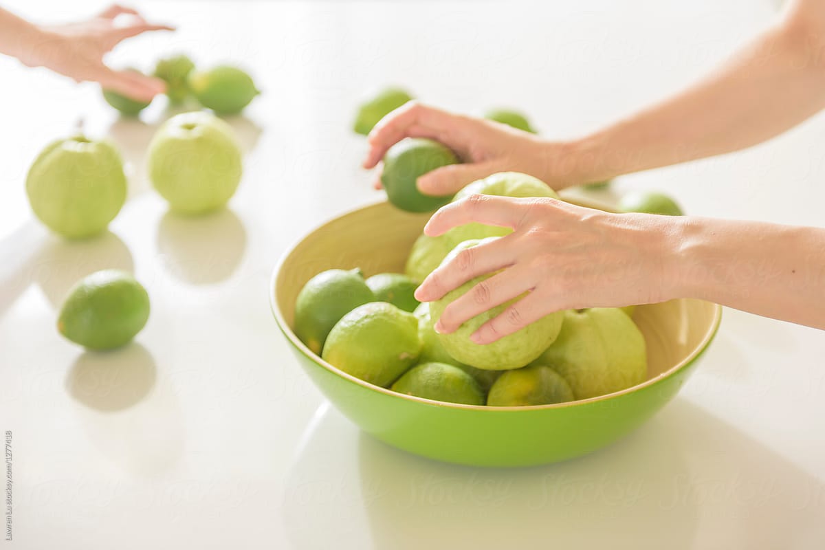 Young woman\'s hands sorting guava and lemon fruit on white kitch