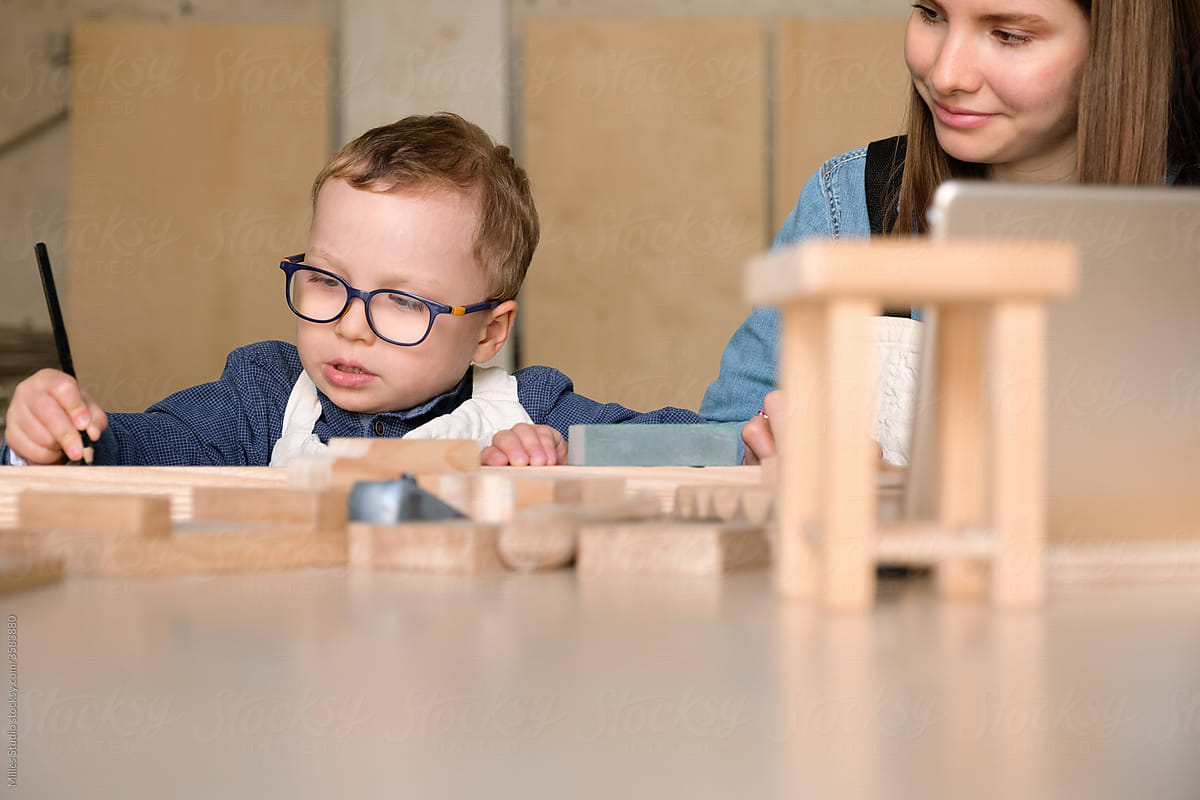 Focused little boy with mom constructing wooden toys in workshop