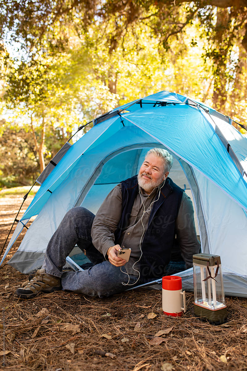 Older Man Uses Headphones While Sitting In His Tent Out In Nature