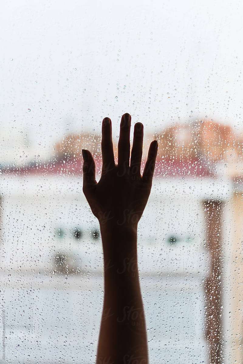 Woman\'s hand on a glass window with raindrops.