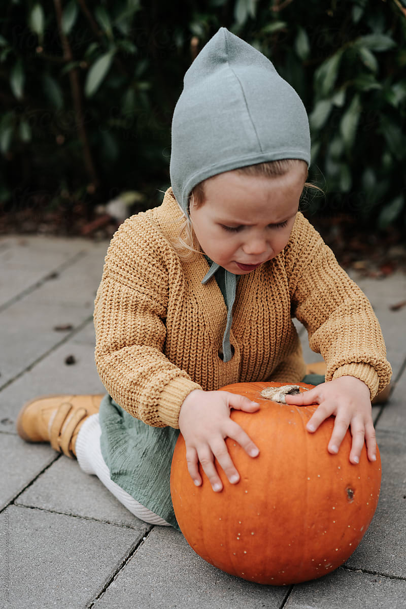 Cute little girl in autumn fashion playing with a pumpkin