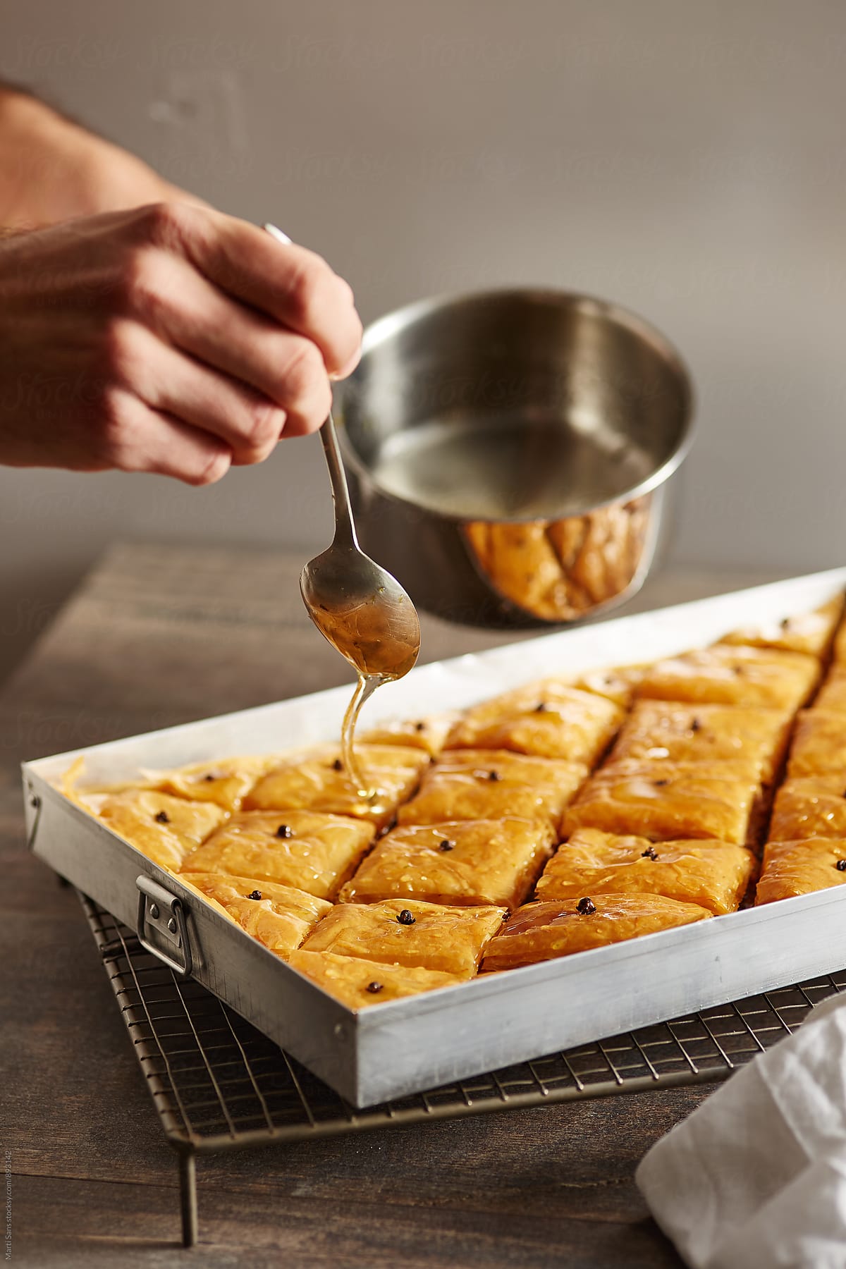 Close-up of man\'s hand covering hot baklava with honey