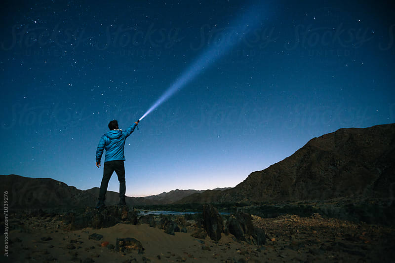 Hiker standing outdoors shining a torch beam into the stars