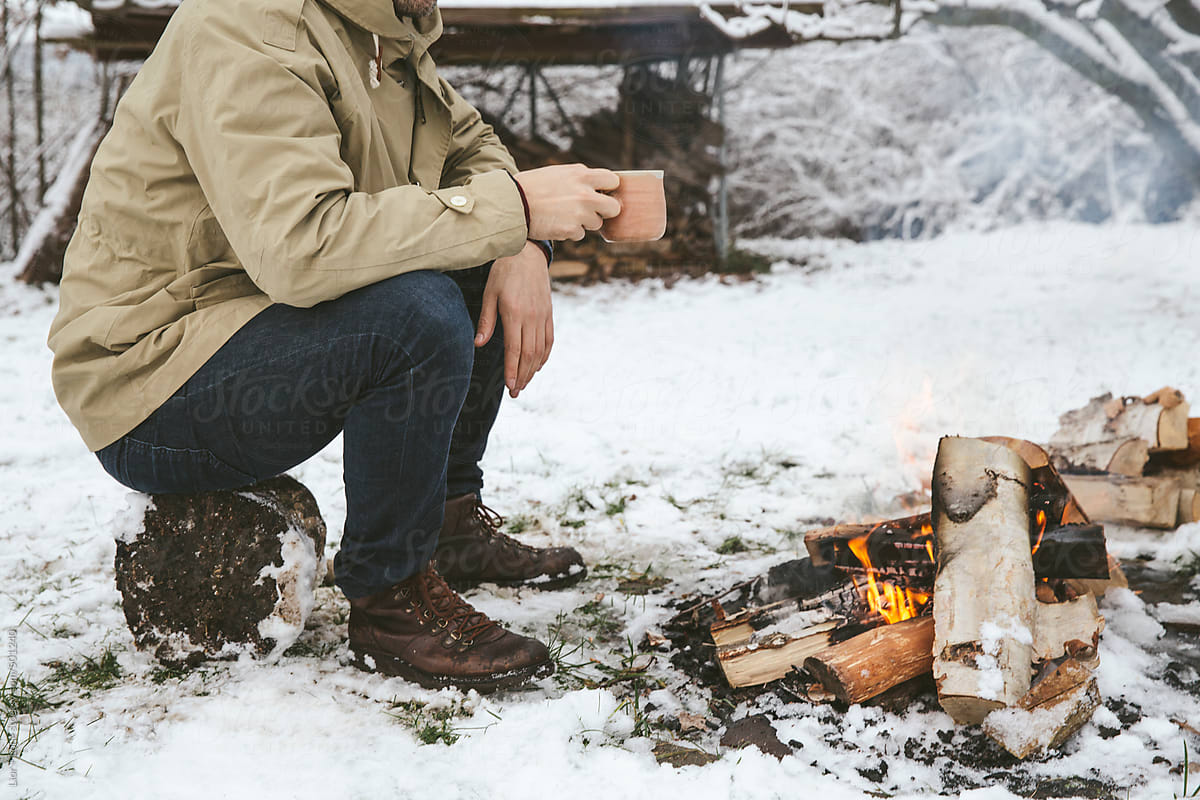 Man having hot drink next to bonfire in the snow