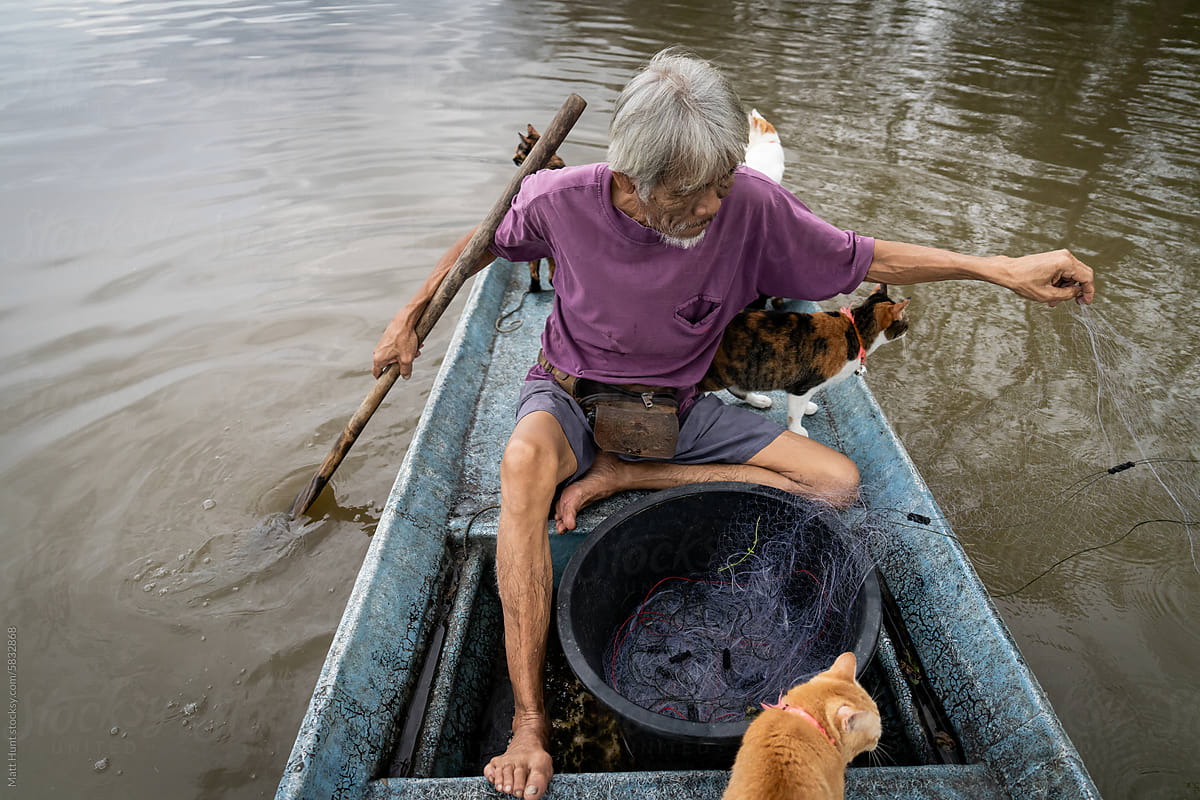 A fisherman releases fishing nets with his cats on a river in Thailand