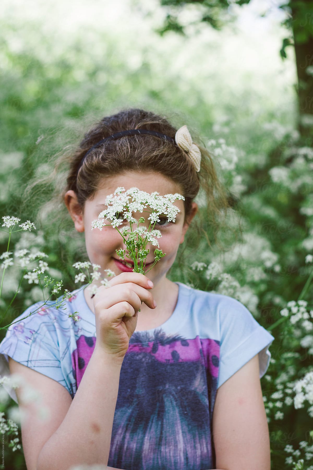A little girl holding a sprig of flowers in front of her face