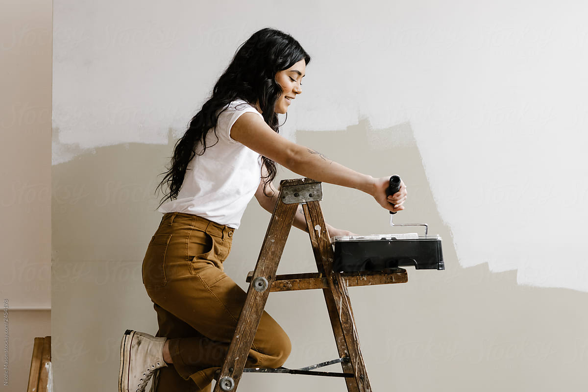 young woman on ladder loading paint on a roller