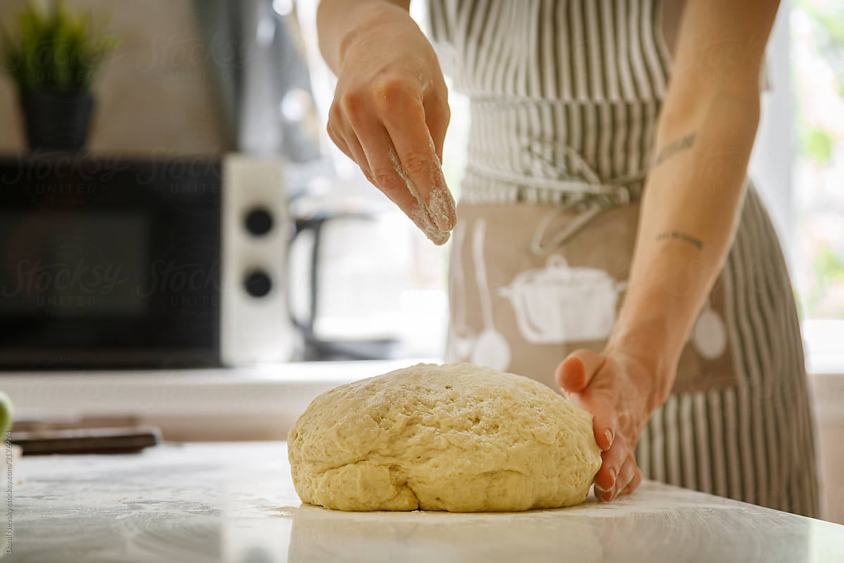 Crop woman sprinkling dough with flour