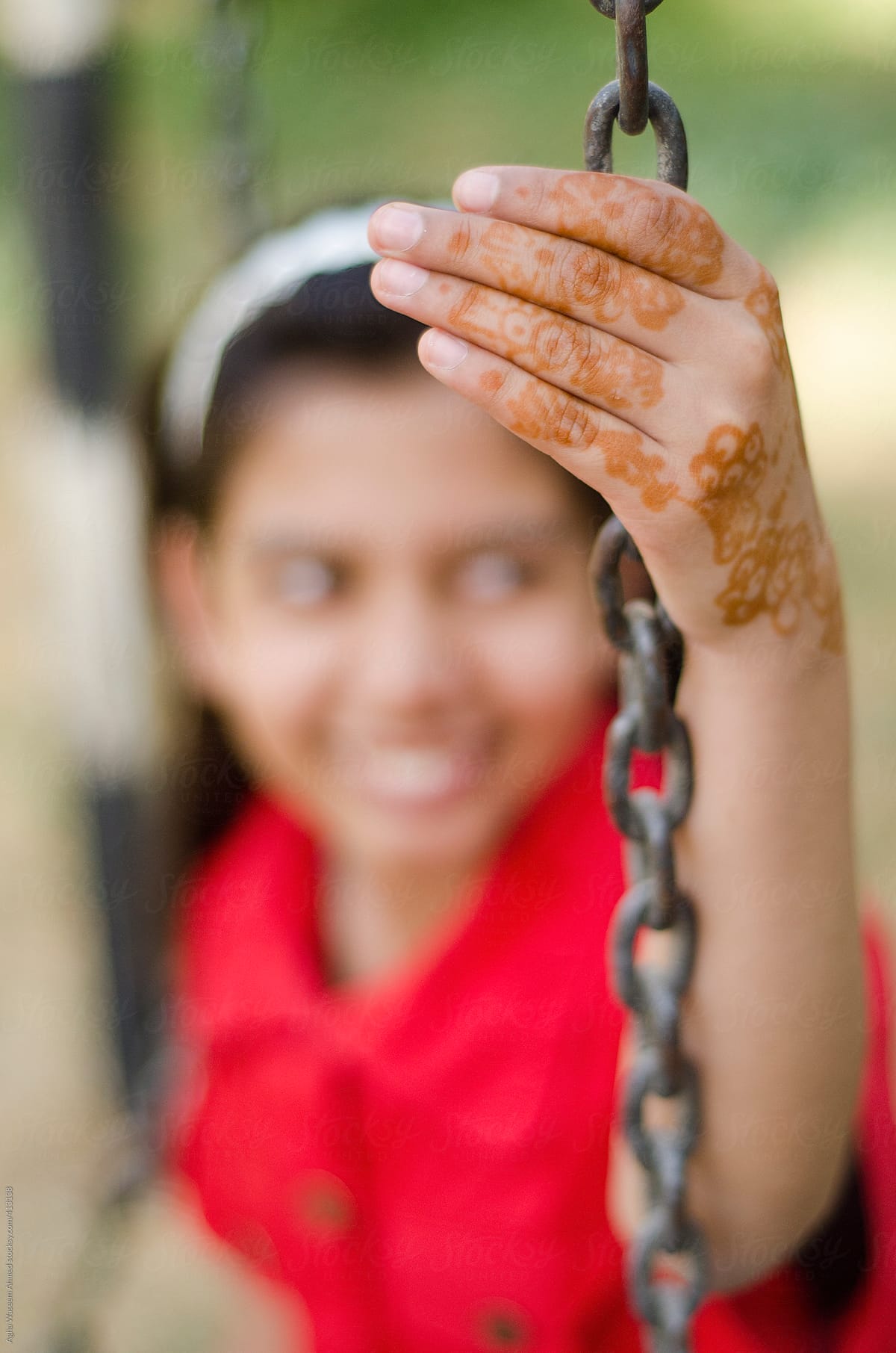 An adolescent girl holding chain of a swing with her henna painted hand