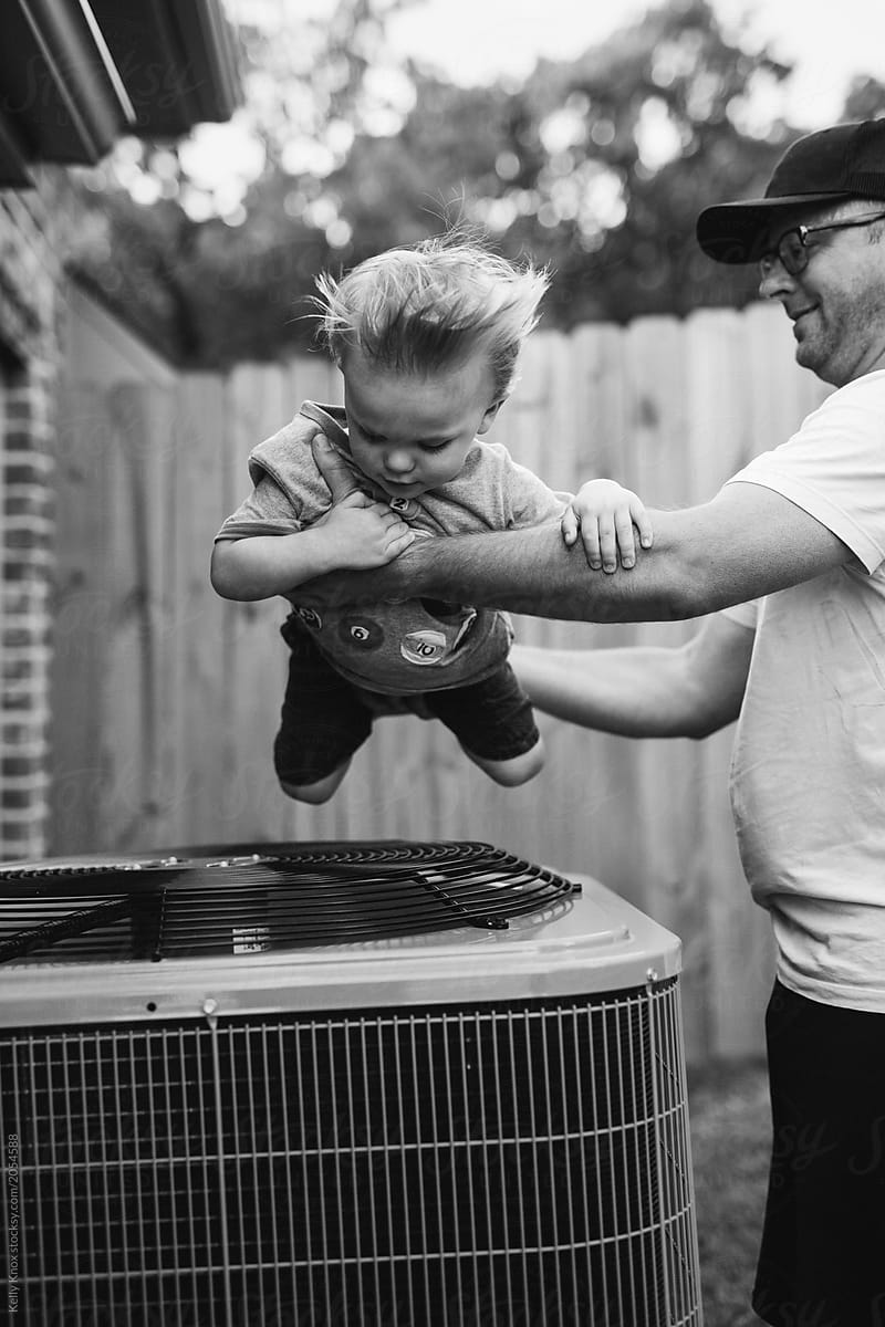 dad flies his toddler son over top of the fan of an air conditioner