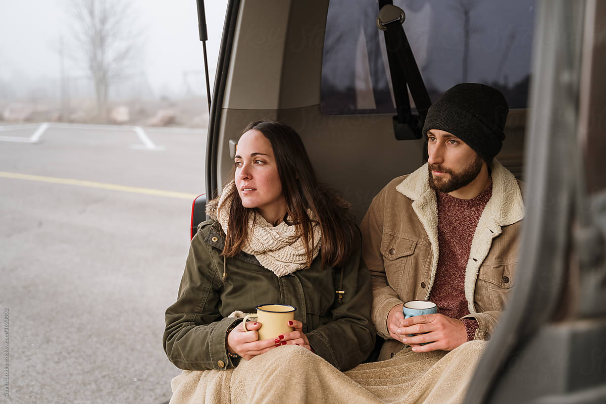 Young couple in a camper van in nature during winter having warm coffe