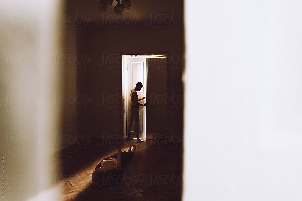 Silhouette of a boy standing near the luminous door and  girl laying on a light