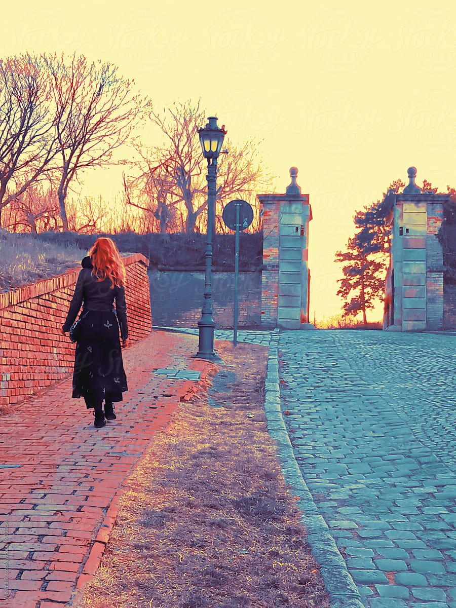 A woman with fiery red hair boldly steps towards an unknown entrance.