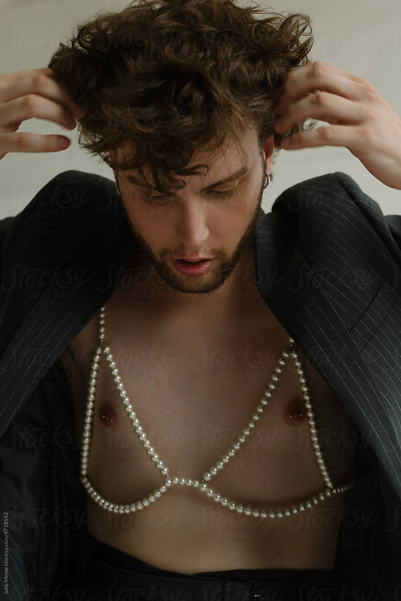 A curly bearded guy in a pearl bra in some thoughts