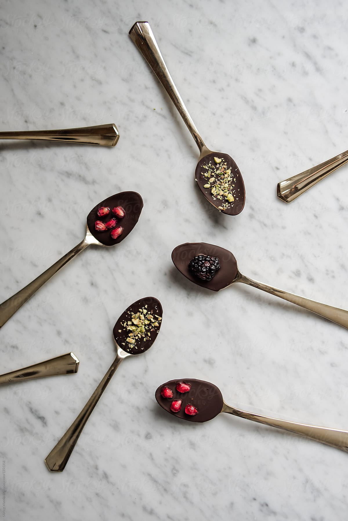 Health dark chocolate covered gold spoons with pomegranate seeds, pistachios and blackberries