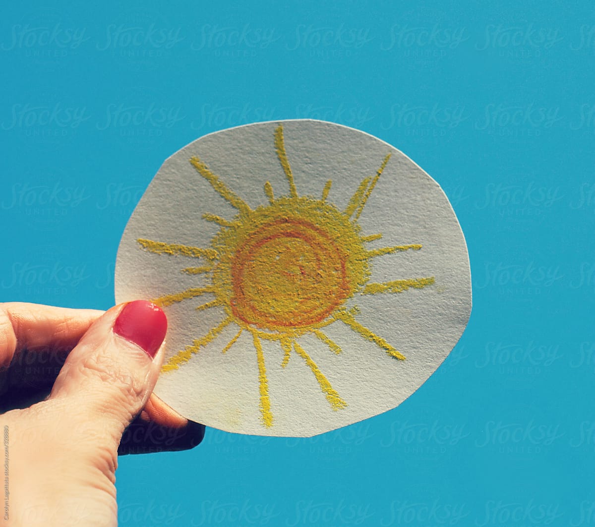 Female holding a drawing of a sun up to the blue sky