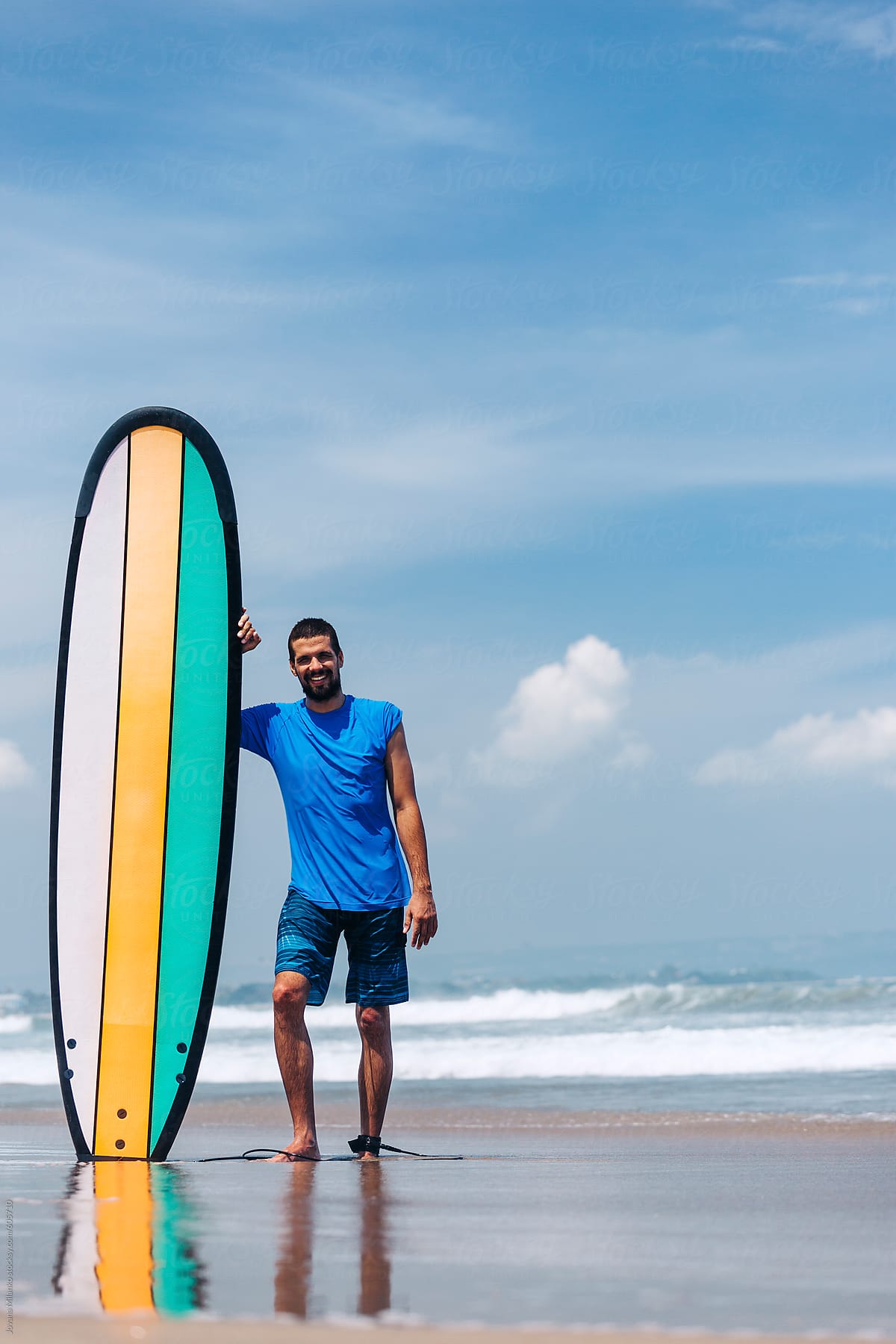 Young surfer standing next to a longboard at a surfing beach