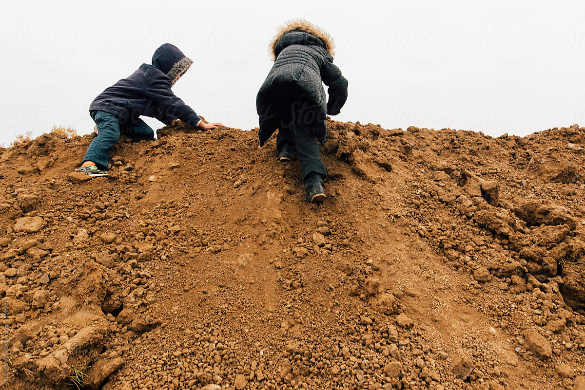 The backside of kids climbing in a dirt pile.
