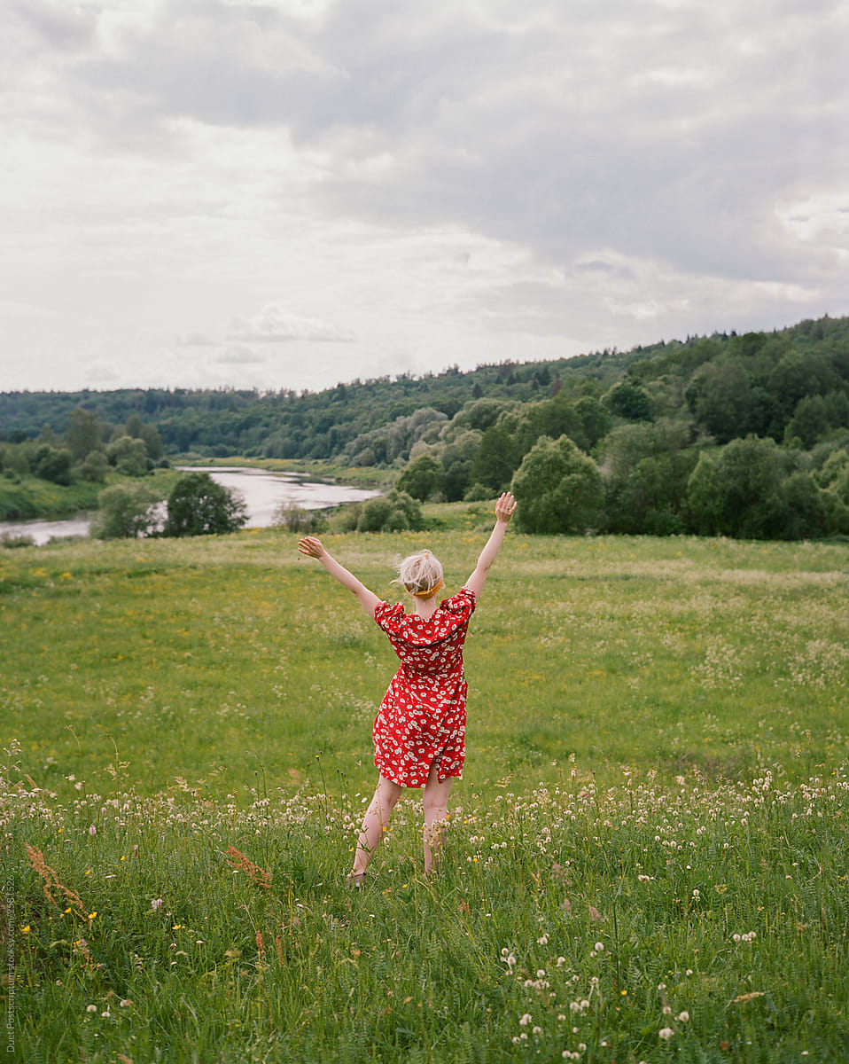 Happy woman in rustic dress holds hands up in beautiful summer field.