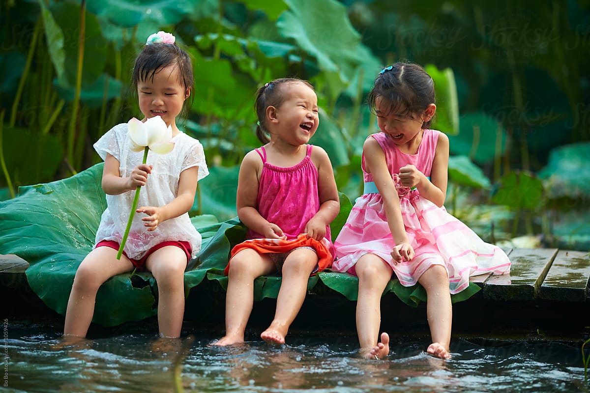 Three little girls sitting by the pond playing water