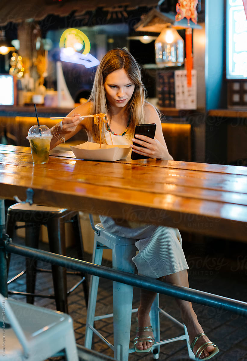 Young woman eating street food while texting.