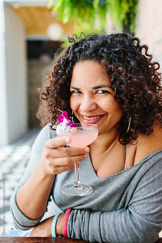 A woman drinking a pink cocktail with a flower in it.