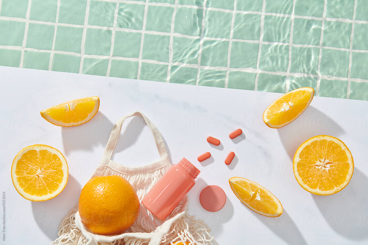 Composition with vitamin C pills, and oranges near pool on