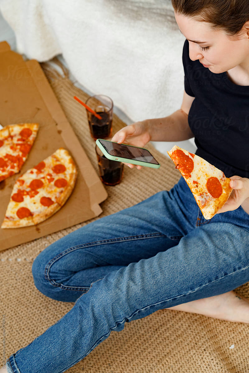 Young woman with pizza using smartphone at home