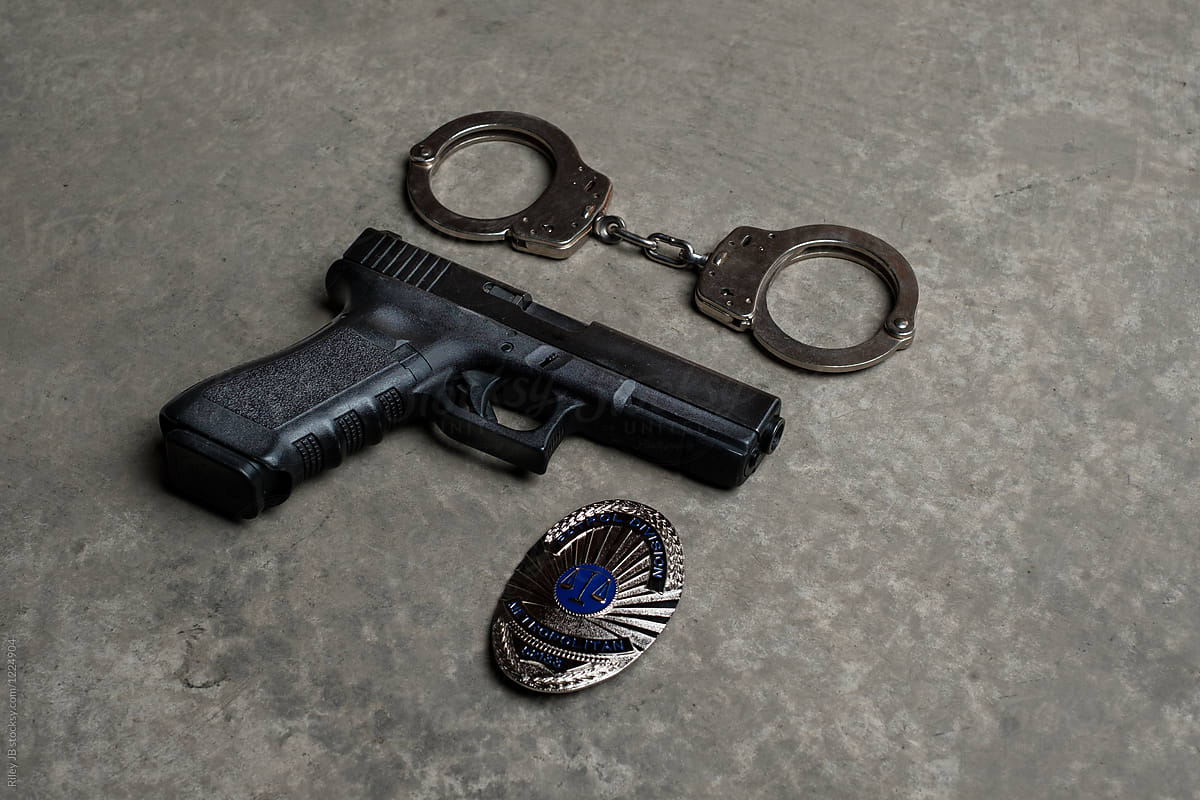 A gun, police badge and handcuffs laying on concrete surface