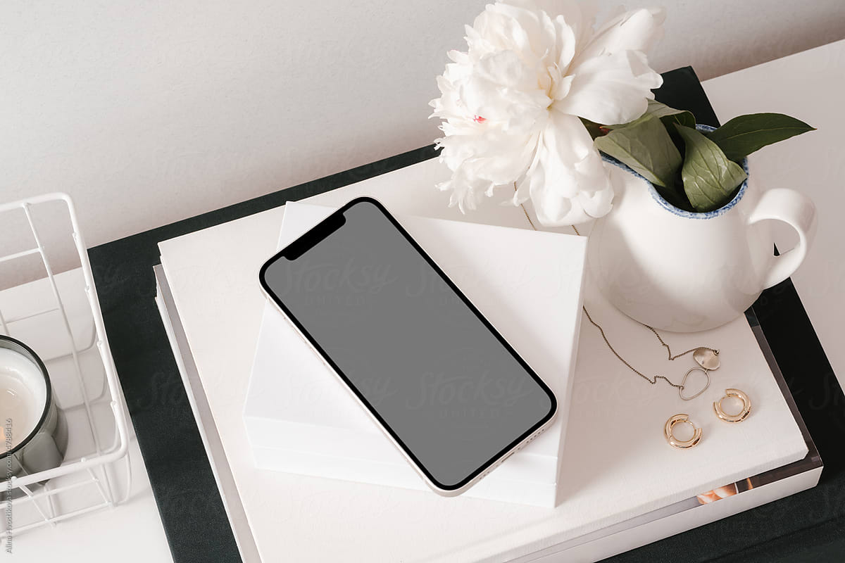 Cellphone with jewelry and flower vase on white desk