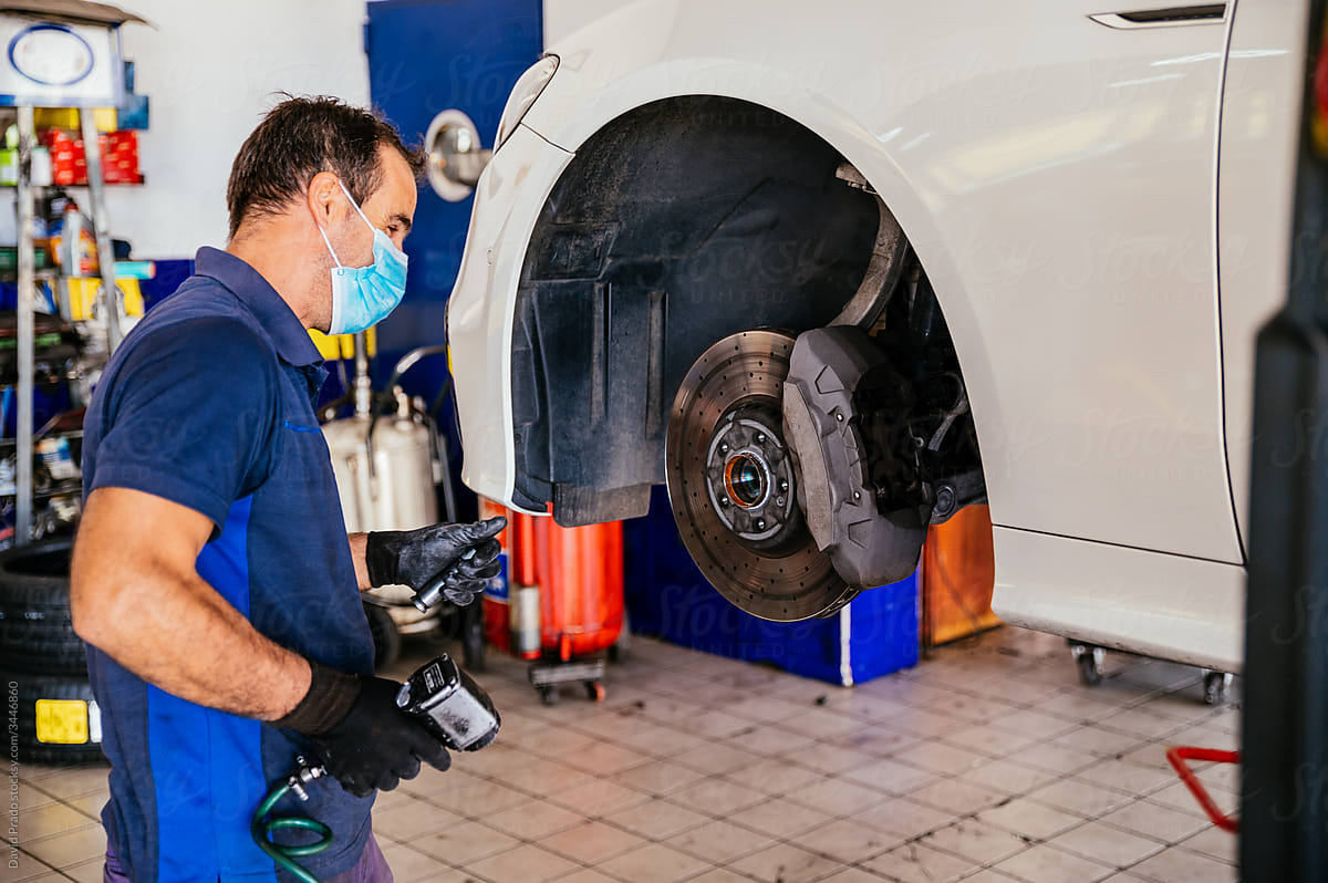 Mechanic in mask screwing wheel to car