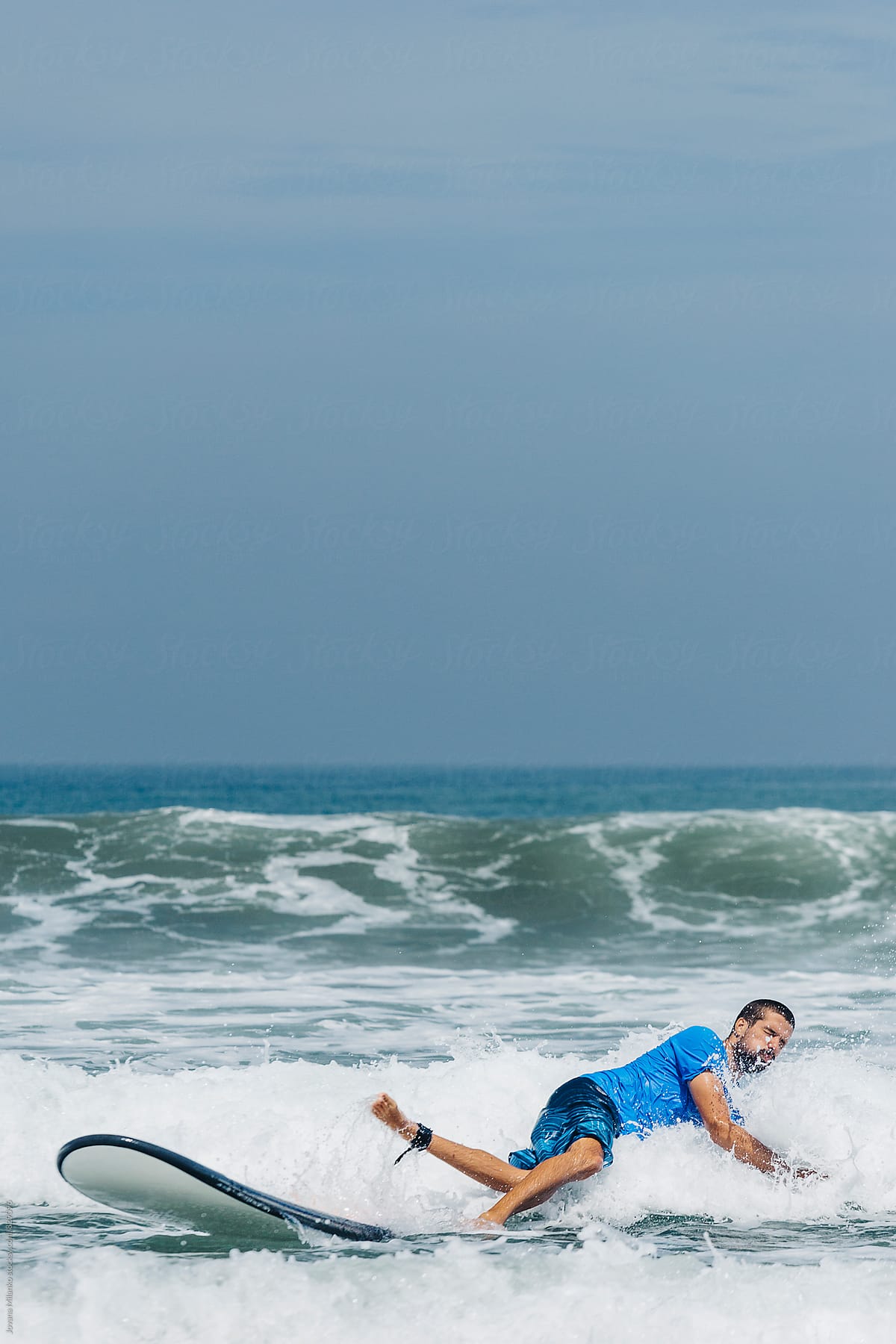 Young man falling in water while learning to surf the waves