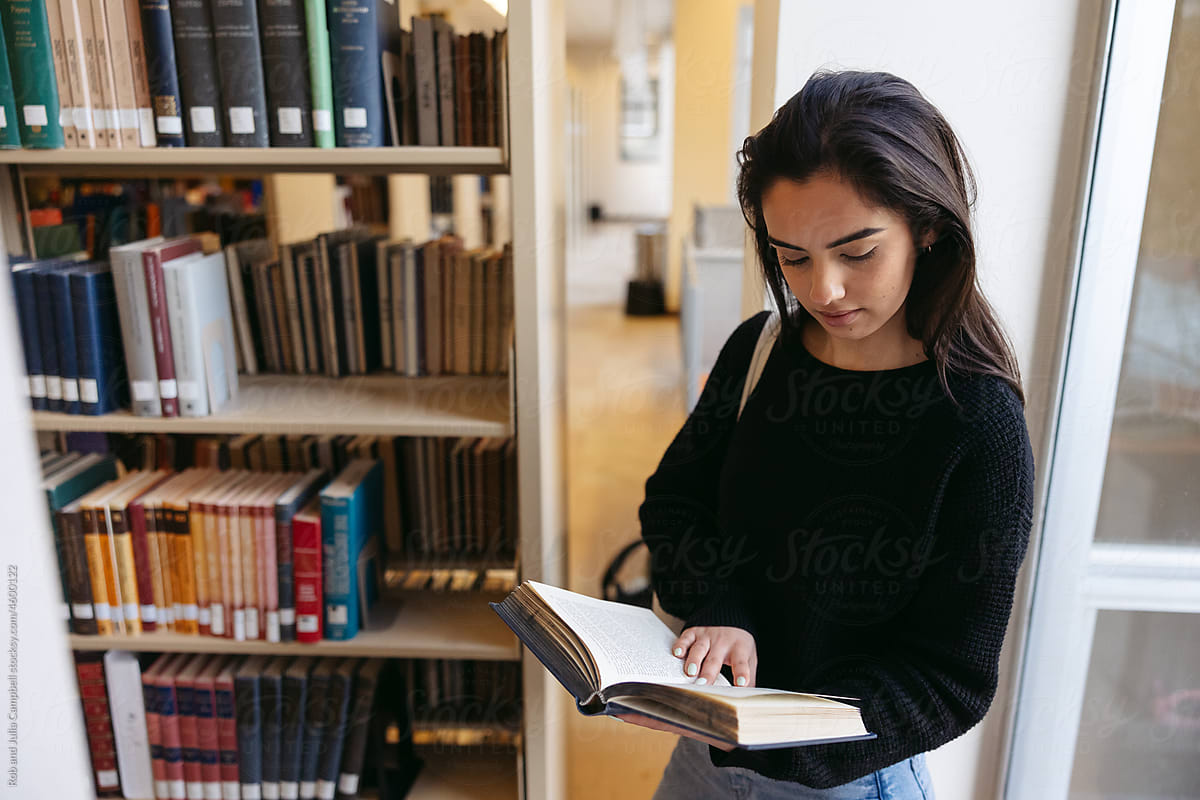 Young woman reading in library at college.