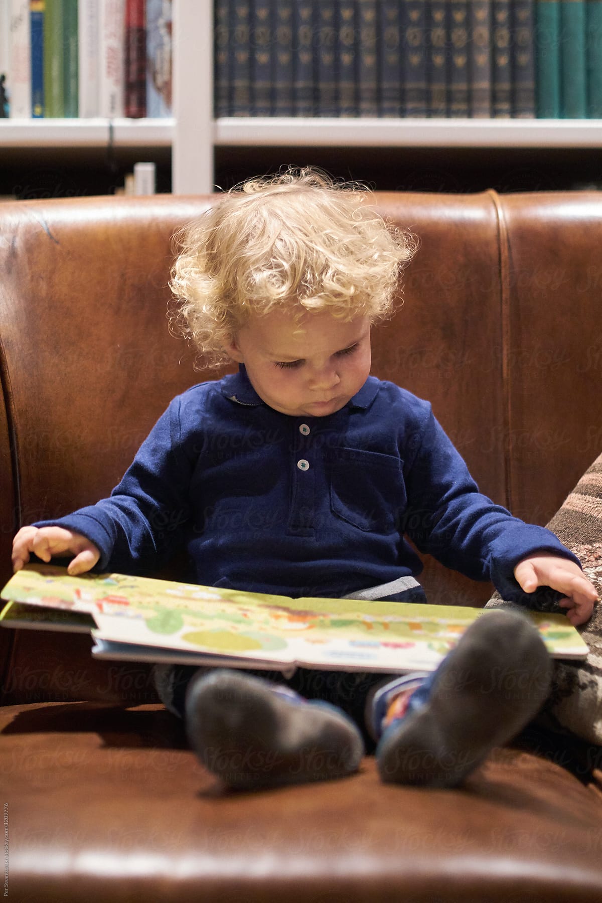 Toddler reading a book in a leather sofa