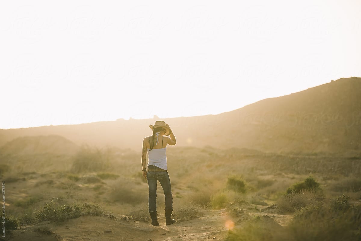 backview of a cowgirl touching his hat in the desert at sunset