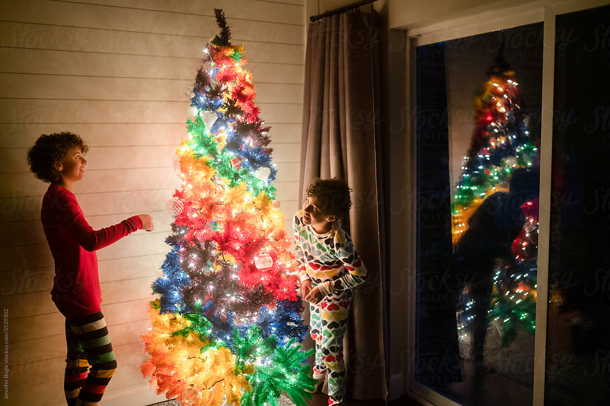 Girl peeks around Christmas tree at brother