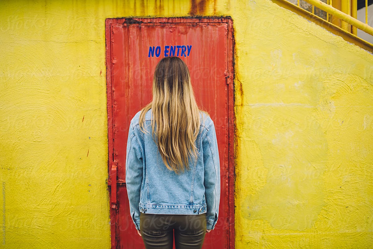 Young woman standing in front of the red door with no entry sign above her