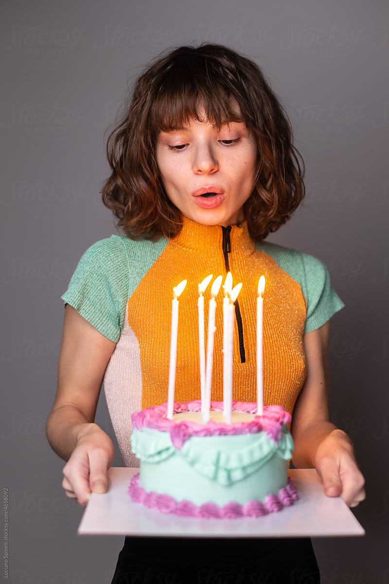 Young woman in orange blowing out long candles on a blue birthday cake
