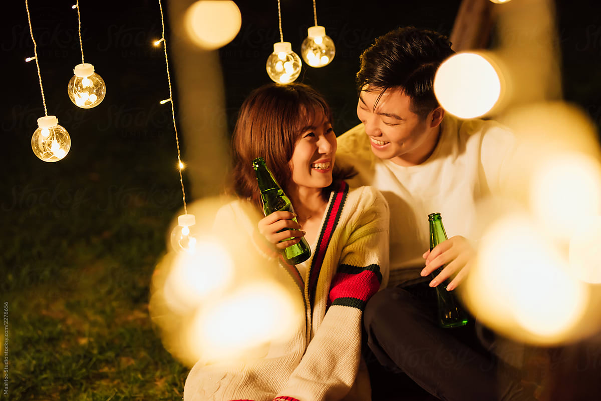 Young couple sitting outdoors, hugging and cheering with beers.