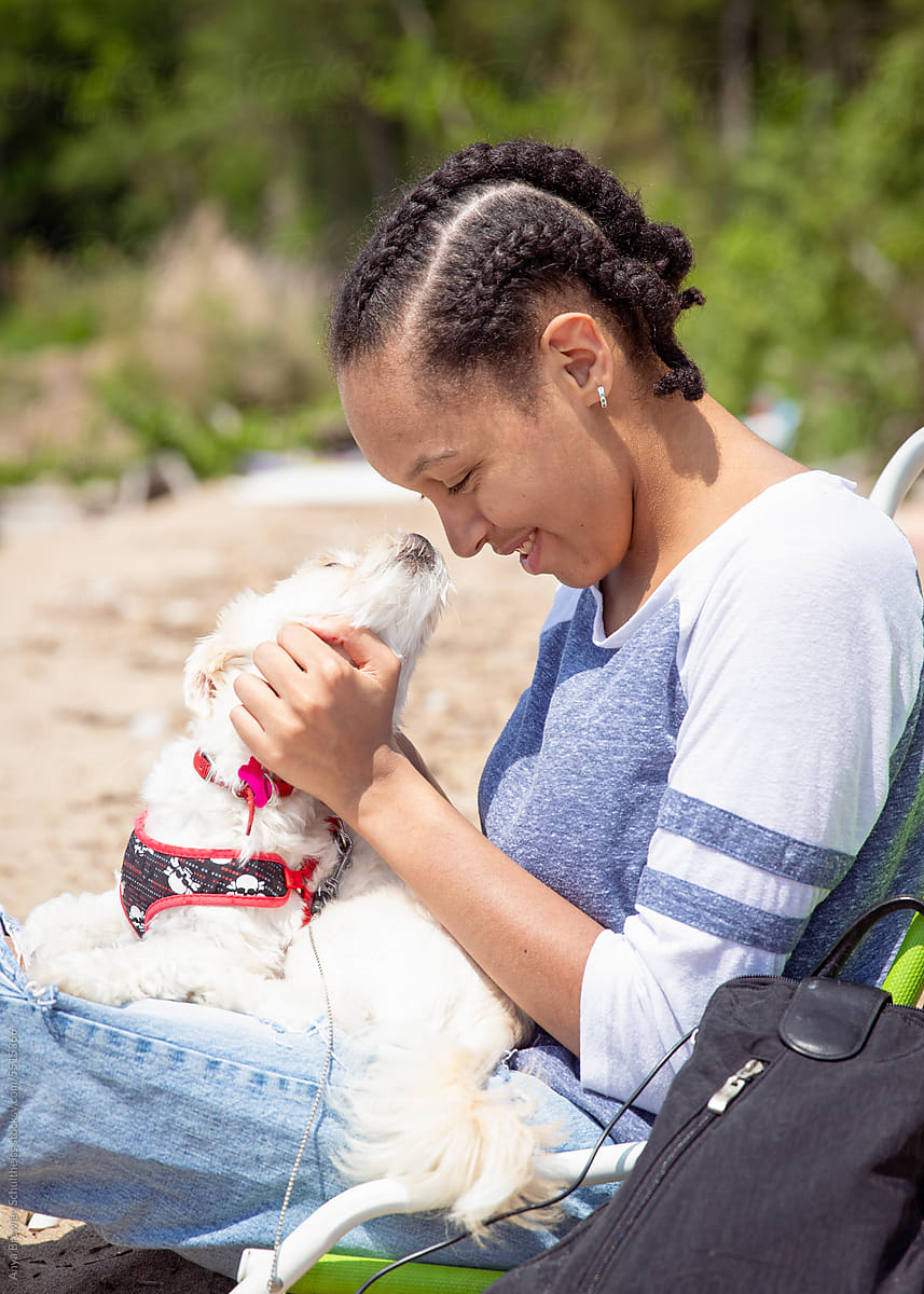 Teenager with cornrow braids smiling with her pet dog at the beach