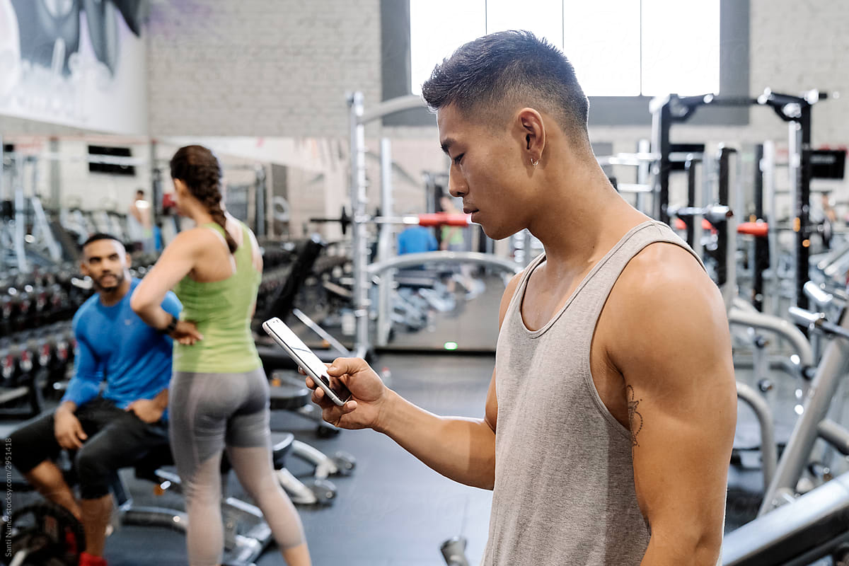 Asian man standing in gym using smartphone..