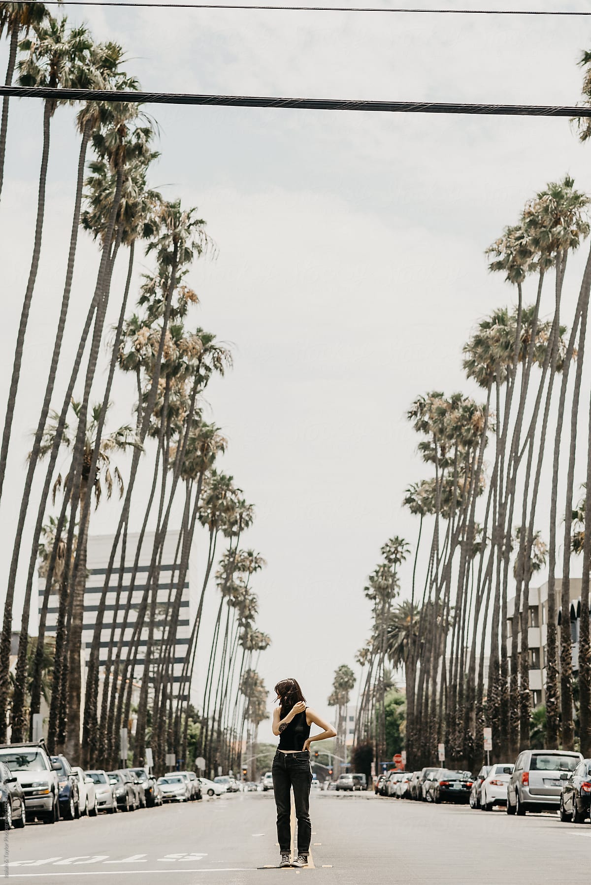 Small woman standing in the middle of a neighborhood street framed by palm trees