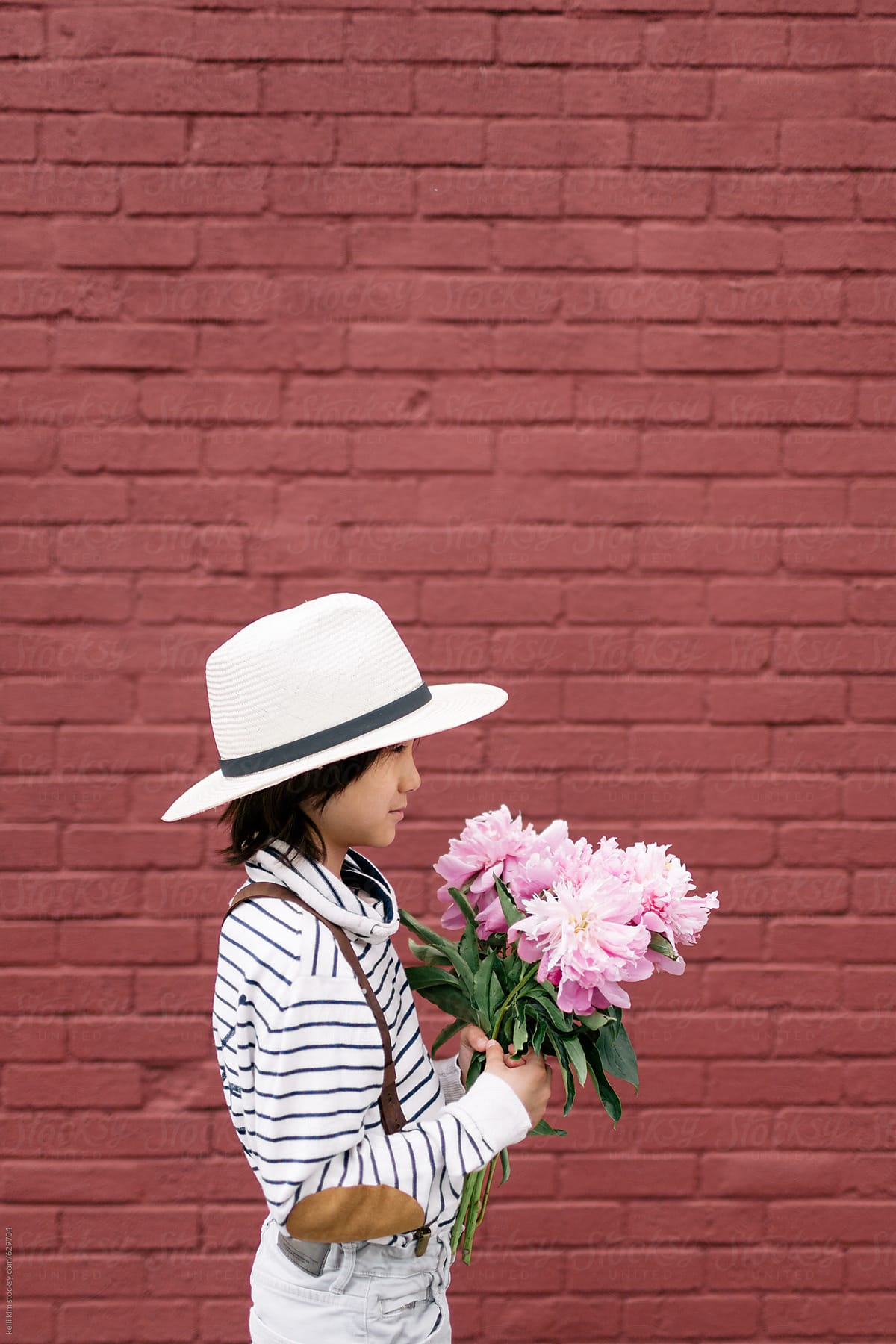 Cute mixed race boy holds pink flowers in front of brick wall