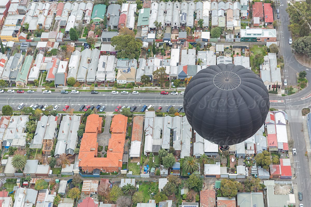 Elevated view of a black hot air ballloon floating across suburban streets